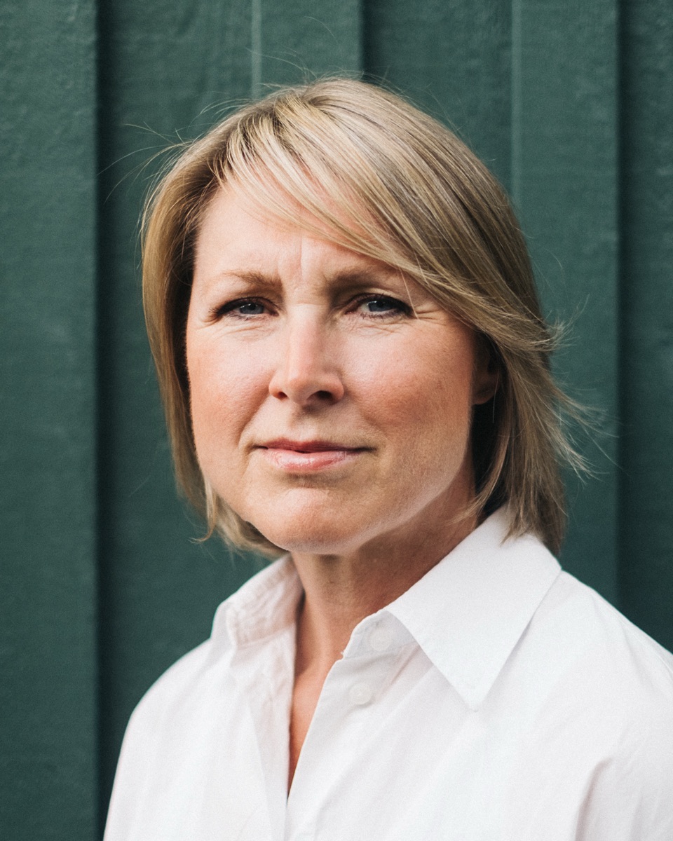 Porträtt av Anna Dahlberg framför en mörkgrön träfasad